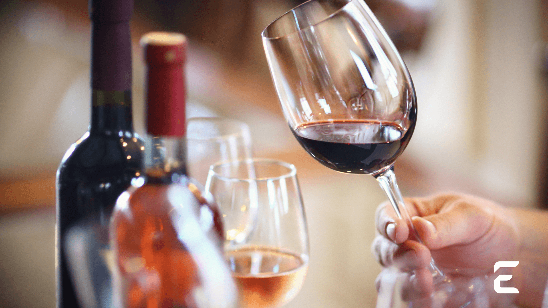Hand swirling red wine in a glass, with bottles in background.